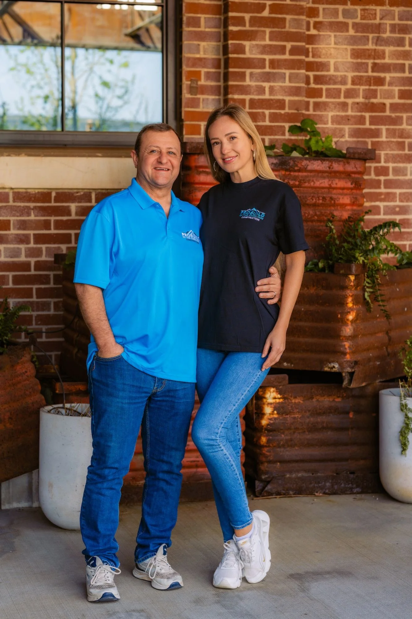 John Clevenger, owner of ProBuild of the Carolinas, and his wife standing together in front of a brick wall